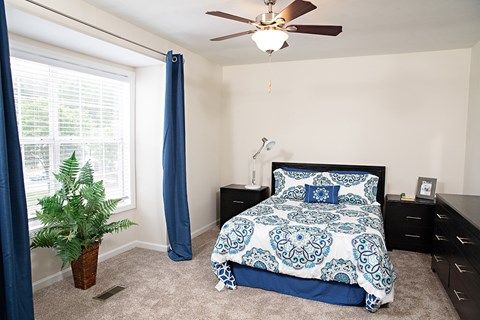 A bedroom with a bed, dresser, and ceiling fan.
