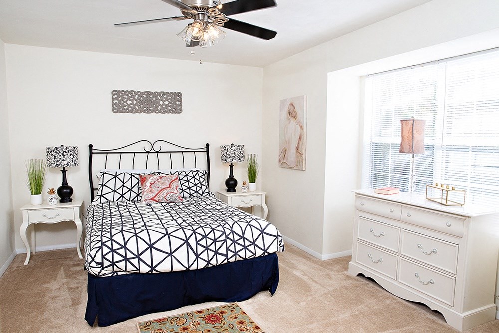 a bedroom with white walls and a black and white bedspread and a white dresser with
