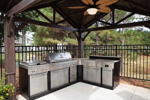 A BBQ grill set up under a wooden pavilion.