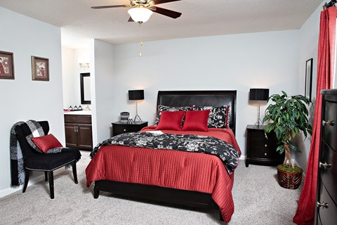 A bedroom with a red bedspread and a black chair.