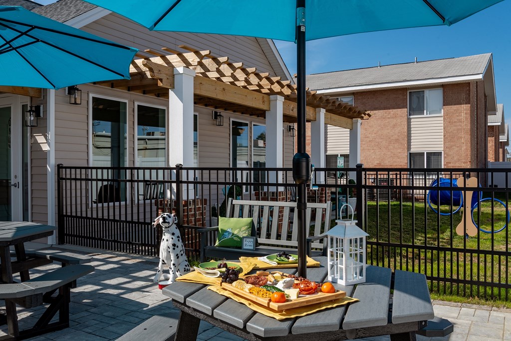 A picnic setup on a patio with a blue umbrella and a tray of food.