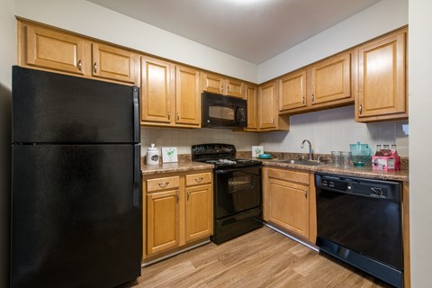 A black refrigerator is in a kitchen with wooden cabinets.