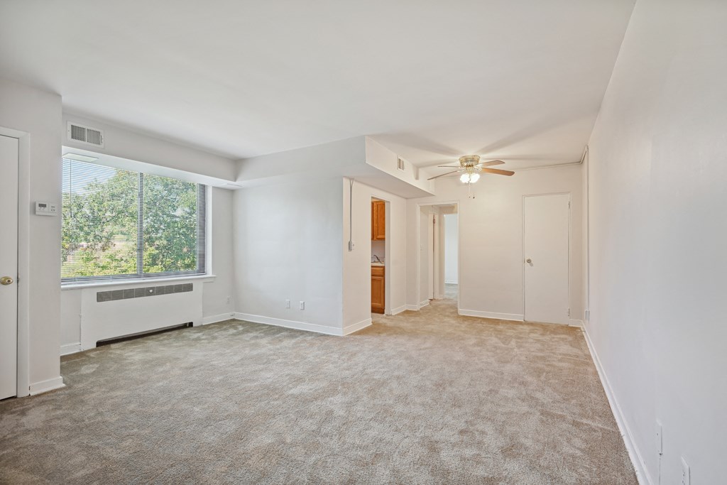 an empty living room with a large window and a ceiling fan
