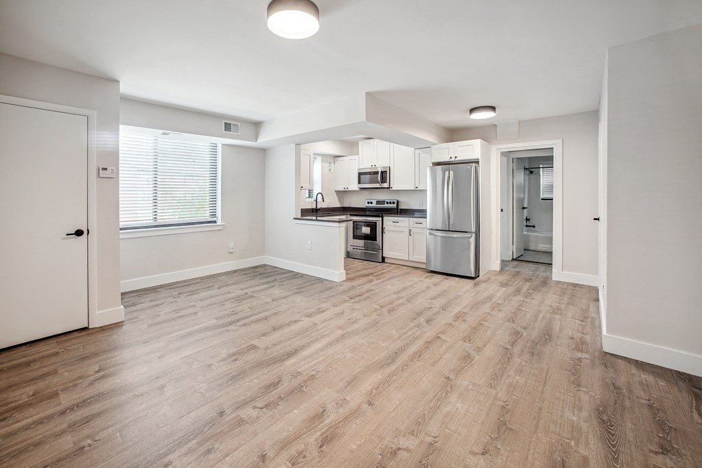 an empty kitchen and living room with hardwood flooring and white walls