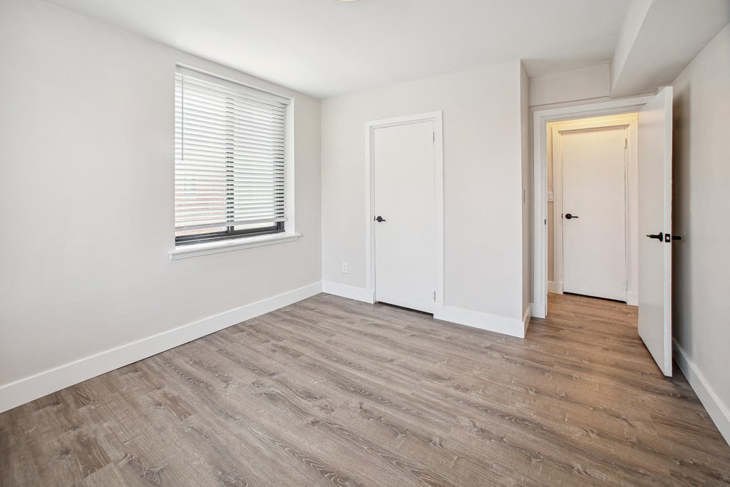 a bedroom with white walls and wood flooring and a window