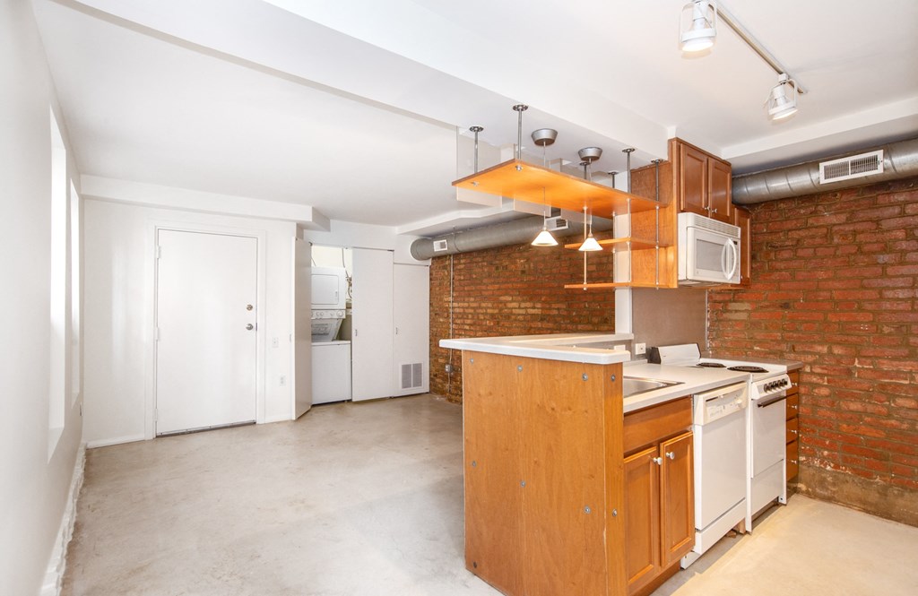 an empty kitchen with white appliances and a brick wall