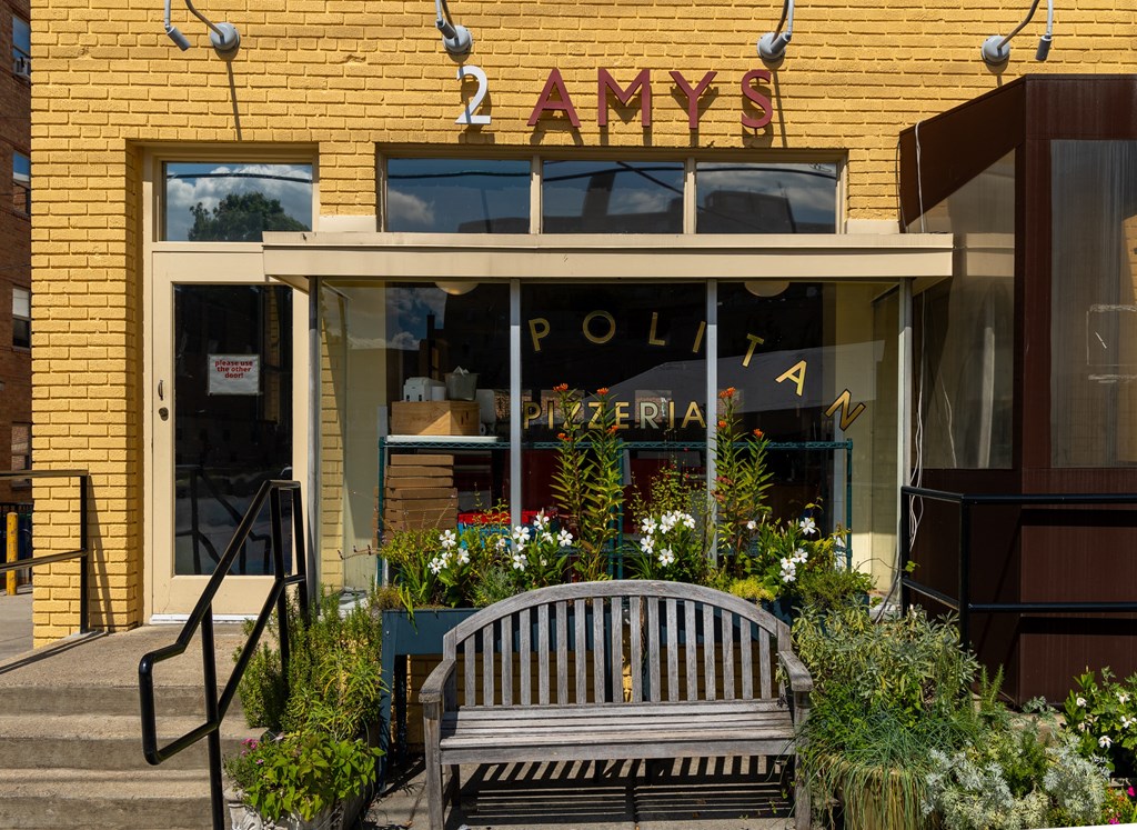 a wooden bench in front of a yellow building with a store window