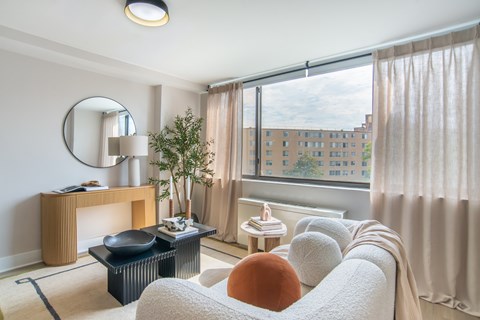 A living room with a large window and a view of a building outside.