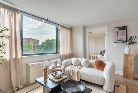 A living room with a white couch and a large window with curtains.