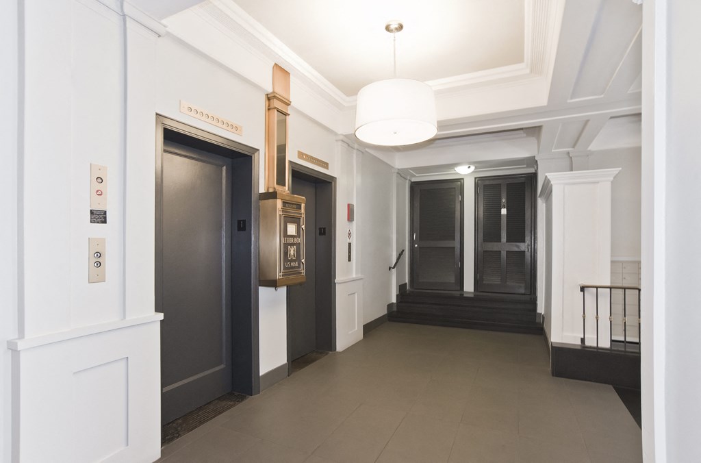 a hallway with three elevators and a white ceiling with a lamp and a door