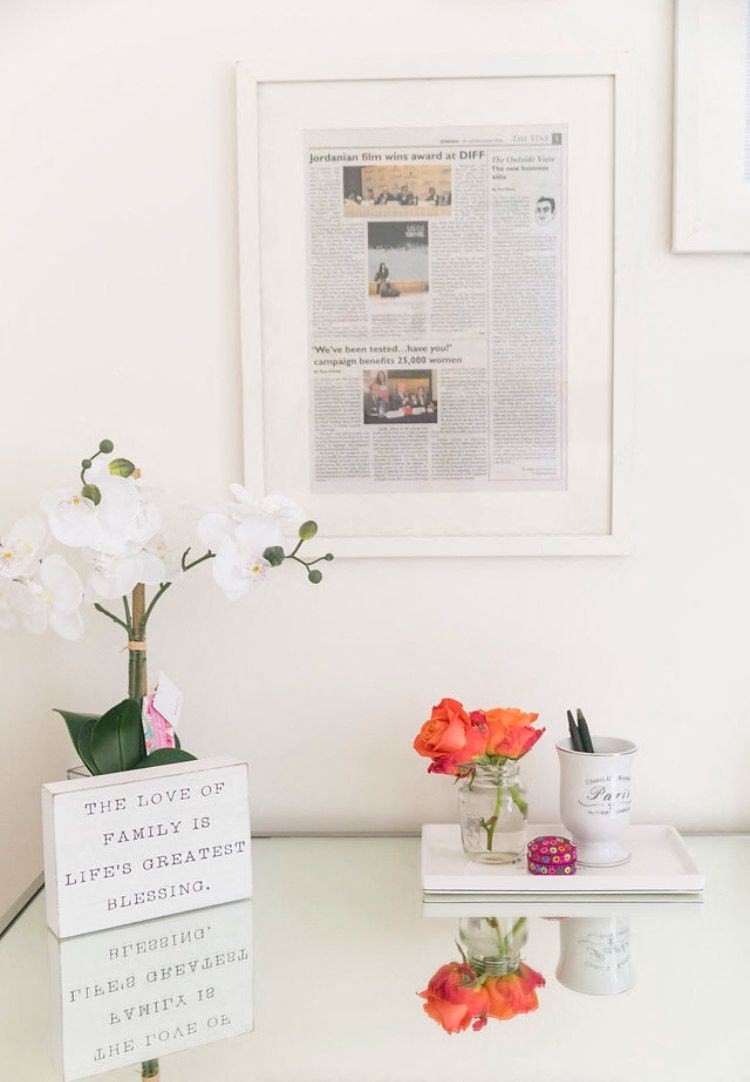 a white desk with flowers and a framed newspaper on the wall