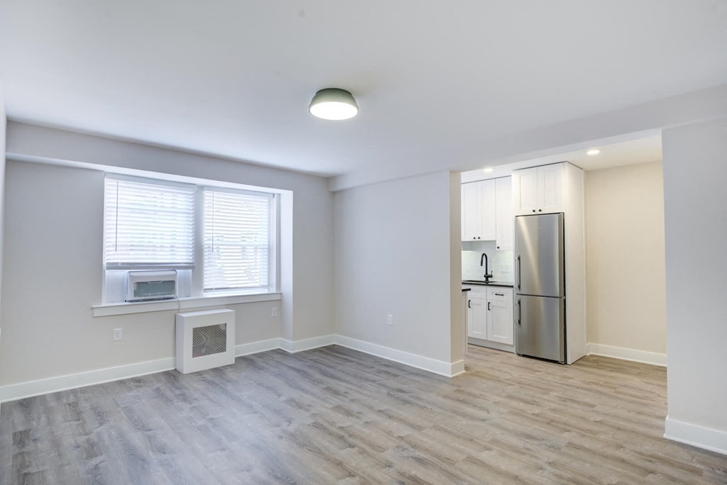 an empty living room with a refrigerator and a window