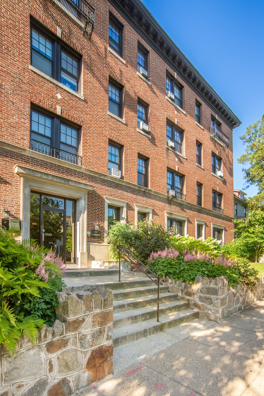 the front of a brick building with stairs and plants