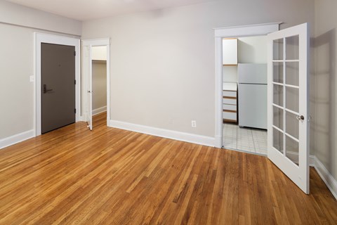 an empty living room with wood flooring and a door to a kitchen