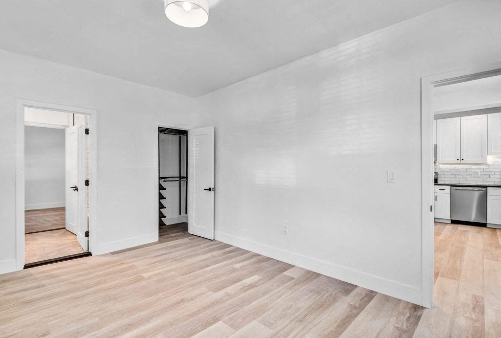 the living room and kitchen of a house with white walls and wood floors