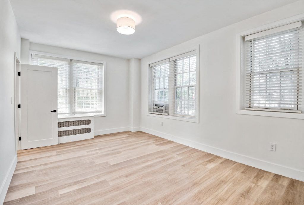 an empty living room with a door and two windows
