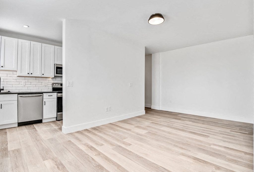 the living room and kitchen of an apartment with white walls and wood floors