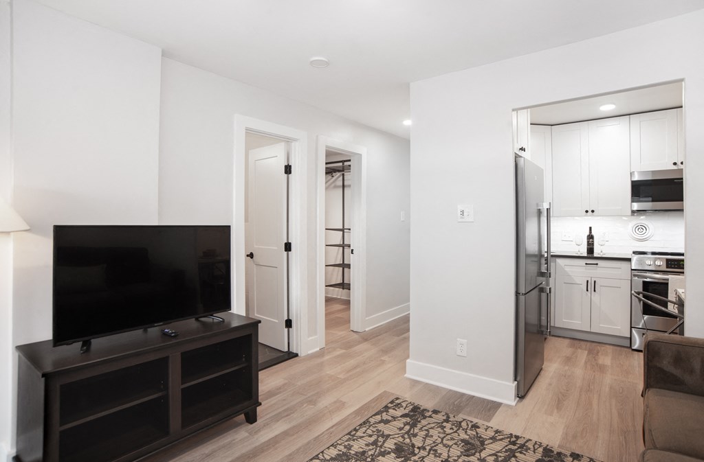 a living room with a tv and a kitchen with a refrigerator