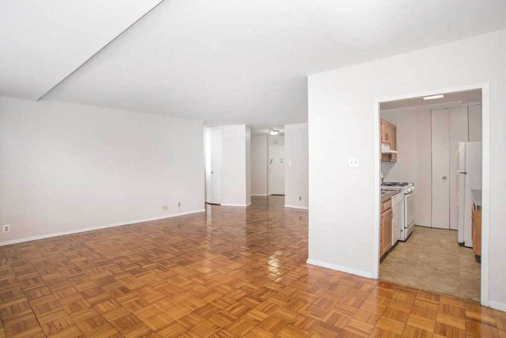 an empty living room and kitchen with wood floors and white walls