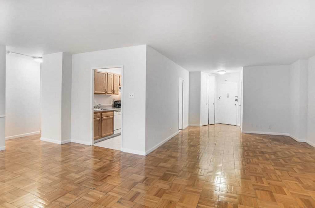 an empty living room with a hard wood floor and a kitchen