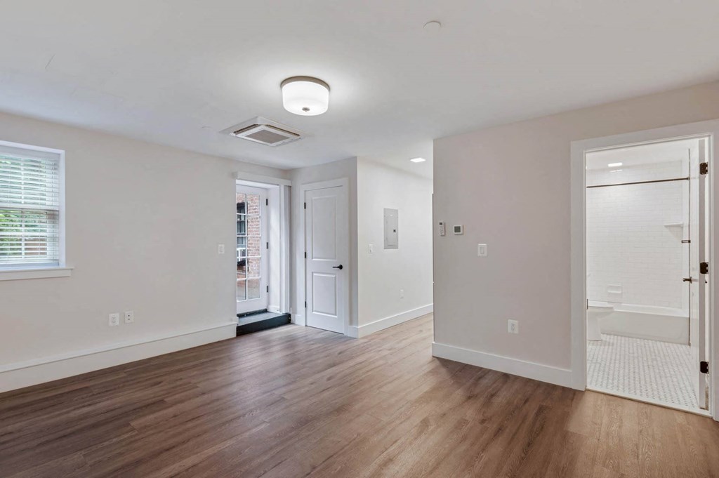 an empty living room with wood floors and a door to a bathroom