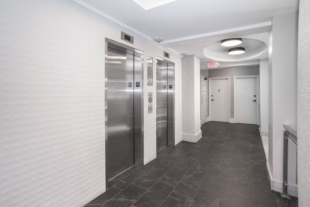 a hallway with stainless steel elevators and white walls