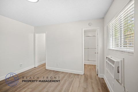 a living room with white walls and wood flooring and a door to a closet