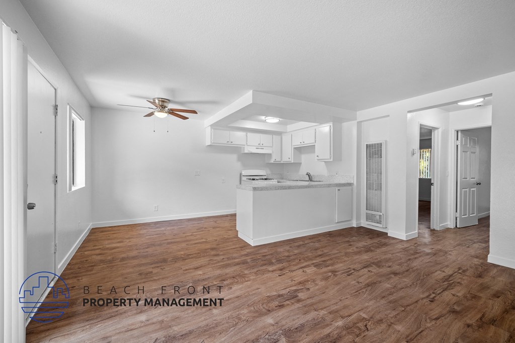 the living room and kitchen of a house with white walls and a wooden floor