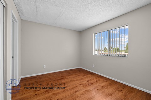 A room with wooden flooring and a window showing a view of trees and a building.