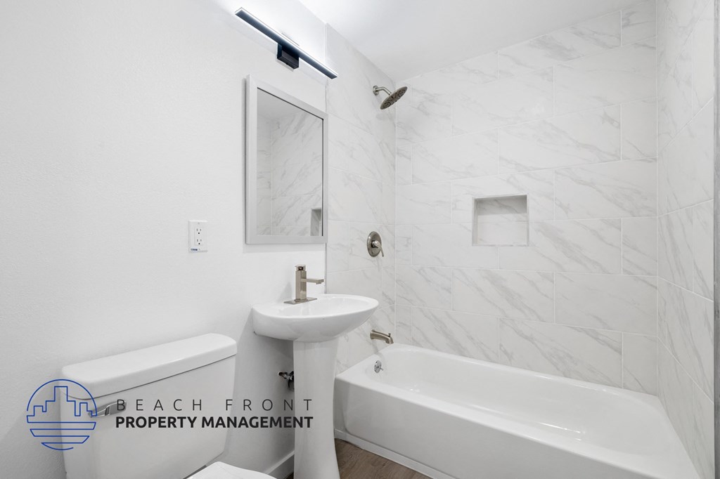 A white bathroom with a marble tile wall and a bathtub.
