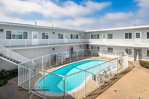 A pool surrounded by a fence in a sunny courtyard.