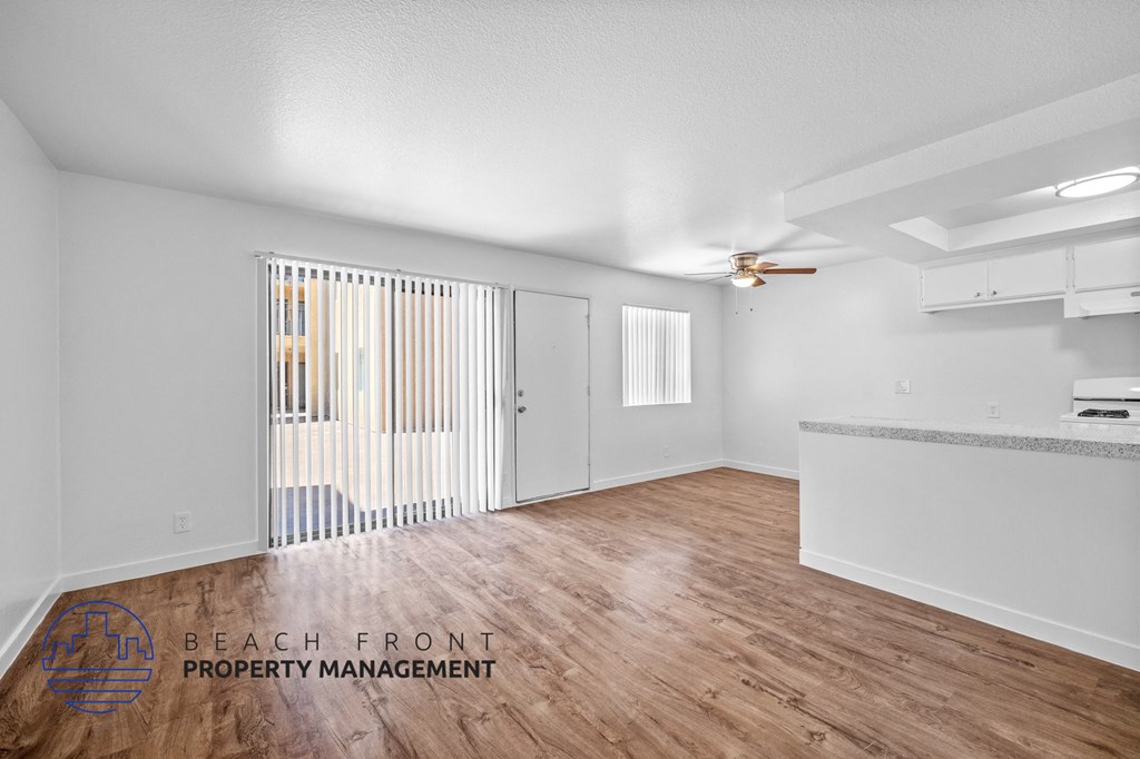 the living room and kitchen of an apartment with wood flooring and white walls