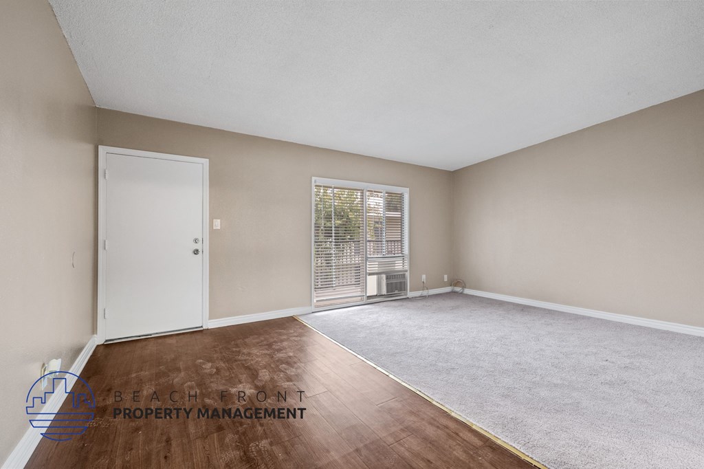 the living room of an apartment with wood flooring and a door to a balcony