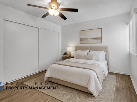 A bedroom with a bed, a ceiling fan, and a painting on the wall.