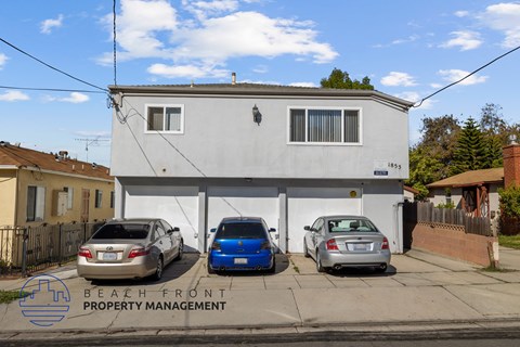 A white building with a sign that says Beach Front Property Management and three cars parked in front.