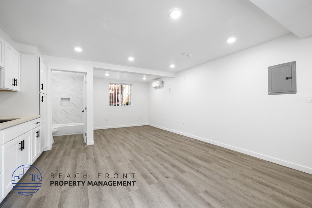 A spacious room with wooden flooring and white walls, with a logo for Beach Front Property Management in the bottom left corner.