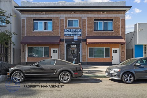 the front of the now leasing building with two cars parked in front
