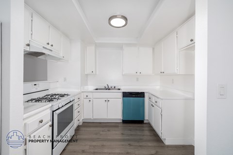 A kitchen with white cabinets and a blue trash can.