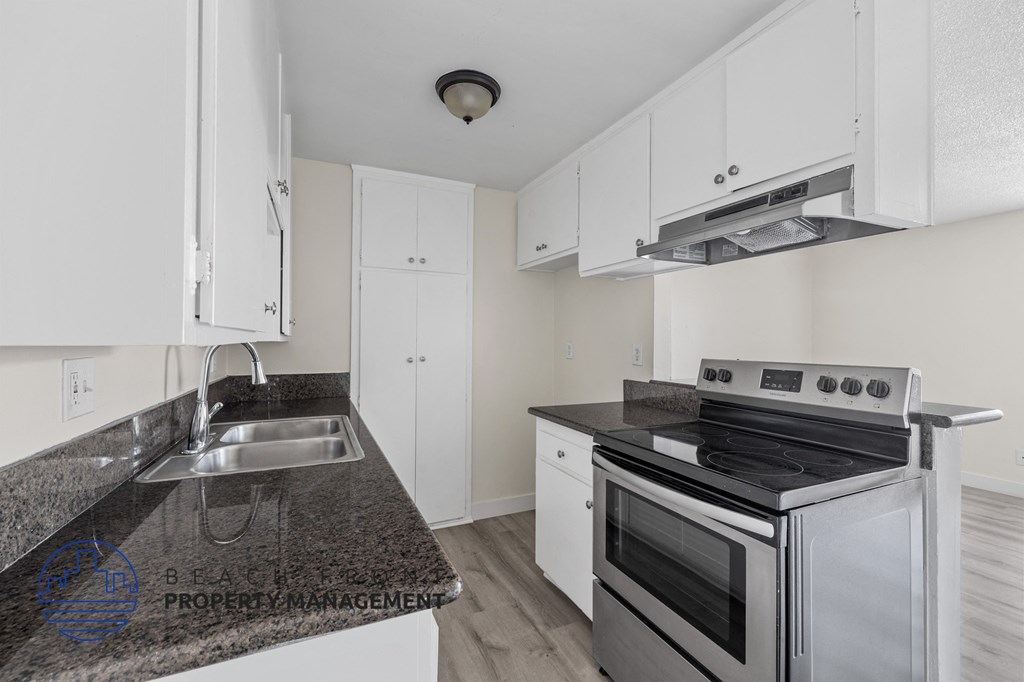 A kitchen with a stove, sink, and cabinets.