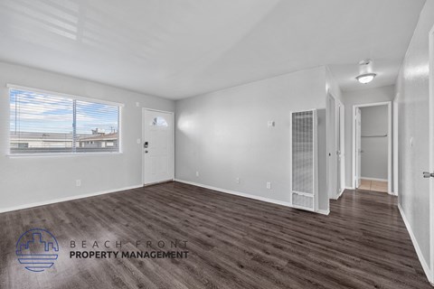 A spacious room with wooden flooring and a large window overlooking a beach.