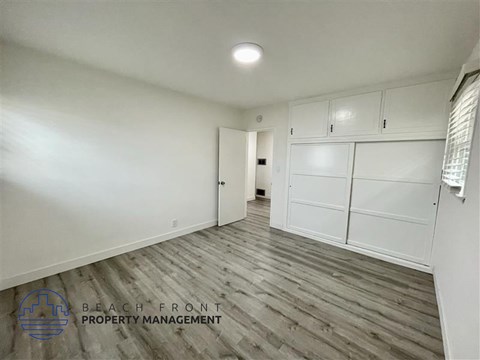 A spacious room with wooden flooring and white walls, managed by Beach Front Property Management.