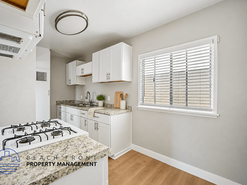 A kitchen with a white stove top oven and white cabinets.