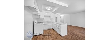 A white kitchen with wooden floors and a logo for Beachfront Property Management in the bottom left corner.