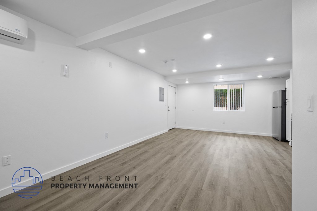 A spacious room with wooden flooring and white walls, with a logo for Beach Front Property Management in the bottom left corner.