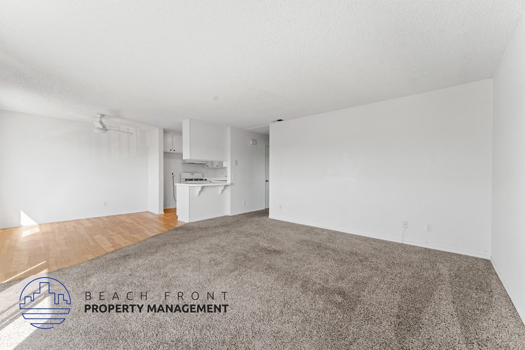 A spacious room with a carpeted floor and white walls, with a logo for Beach Front Property Management in the bottom left corner.