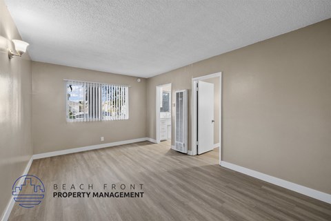 A spacious room with wooden flooring and a refrigerator in the corner.