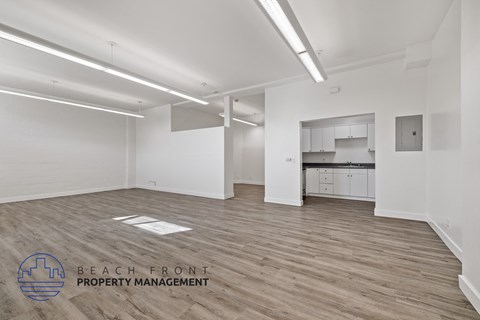 A spacious room with wooden flooring and white walls, with a logo for Beach Front Property Management in the bottom left corner.