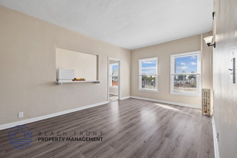 A spacious room with wooden flooring and a view of the beach through the windows.