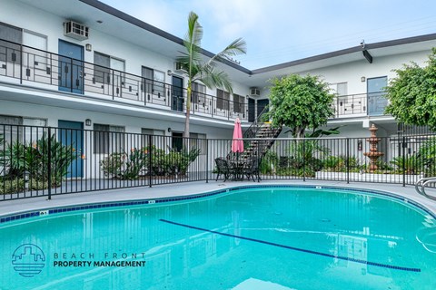 A swimming pool is surrounded by a black fence and a building with balconies.