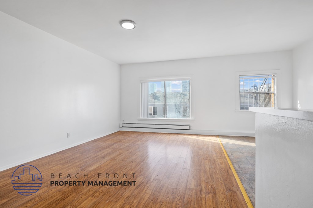 A room with wooden flooring and two windows, one of which has a view of a construction site.